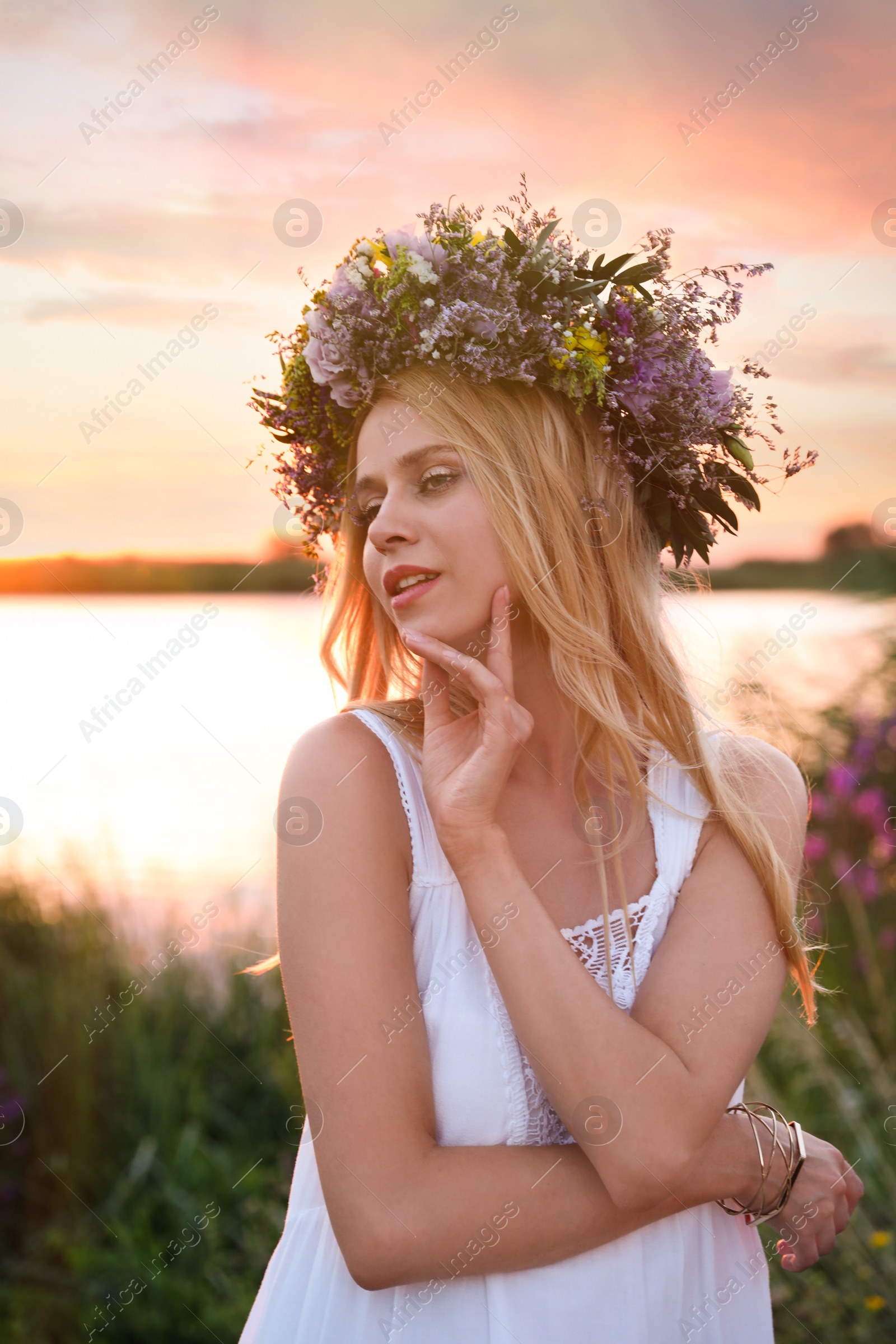 Photo of Young woman wearing wreath made of beautiful flowers outdoors at sunset