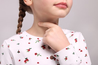 Photo of Girl suffering from sore throat on light grey background, closeup