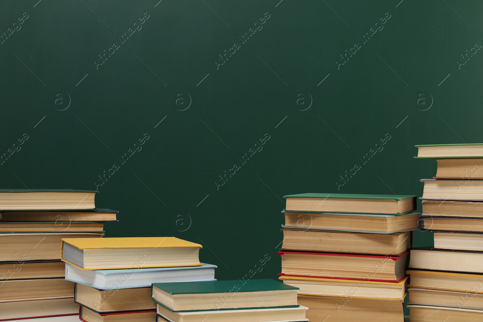 Photo of Many hardcover books near green chalkboard, space for text. Library material