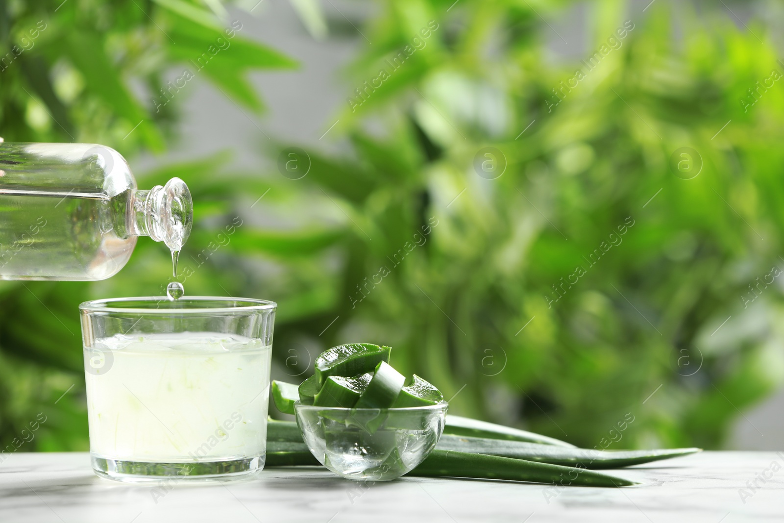 Photo of Pouring aloe vera juice from bottle into glass on table against blurred background. Space for text