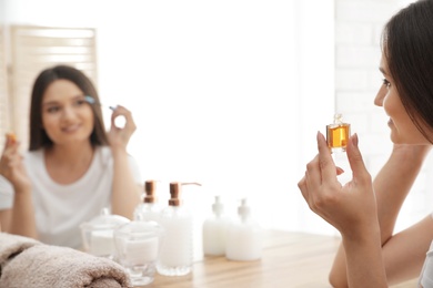 Photo of Beautiful woman applying oil onto her eyelashes near mirror indoors