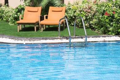 Photo of Sunbeds near modern swimming pool with stairs, outdoors