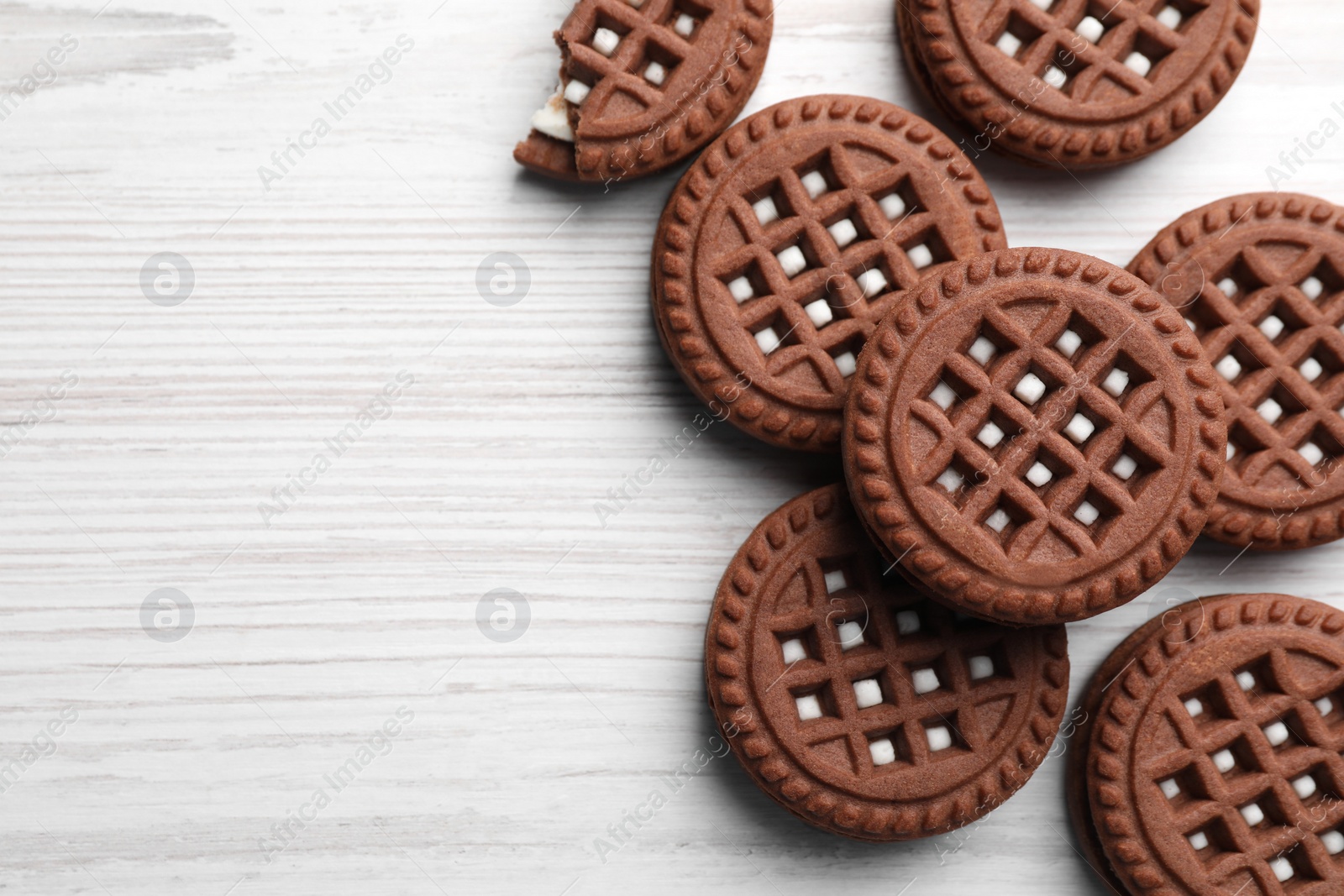 Photo of Tasty chocolate sandwich cookies with cream on white wooden table, flat lay. Space for text