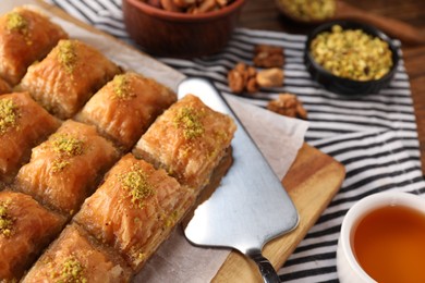 Photo of Delicious sweet baklava with pistachios and cake server on table, closeup