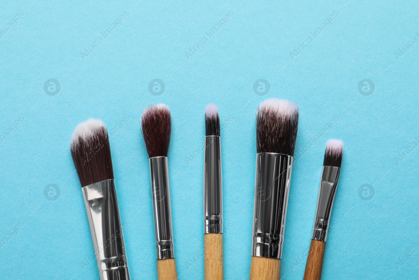 Photo of Different makeup brushes on light blue background, flat lay. Space for text