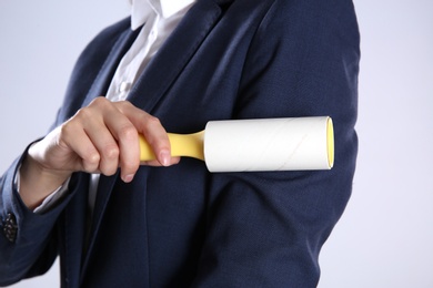 Woman cleaning dark blue jacket with lint roller on grey background, closeup