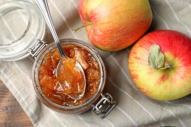 Photo of Tasty apple jam in glass jar and fresh fruits on wooden table, flat lay
