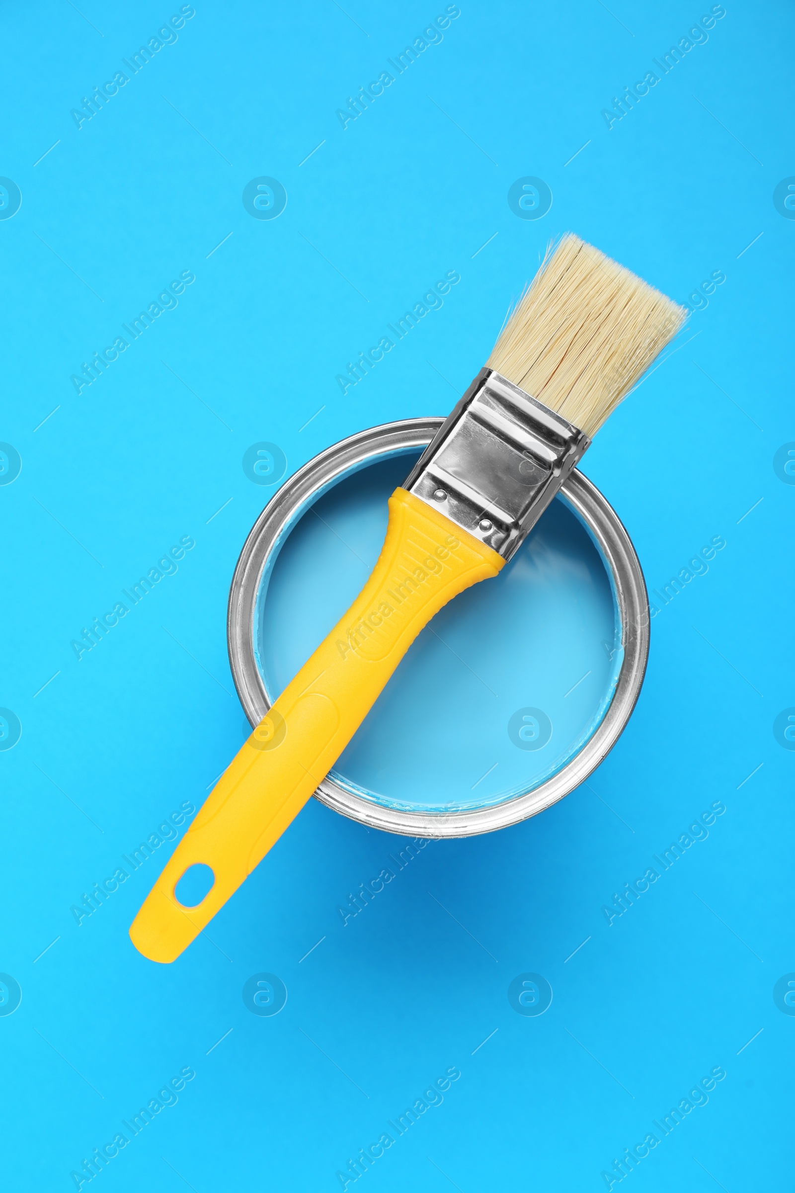 Photo of Can of paint with brush on light blue background, top view