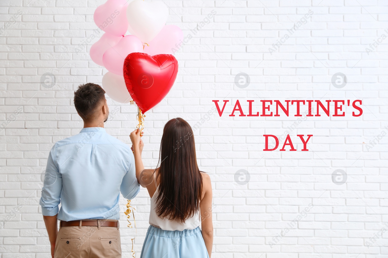 Photo of Young couple with air balloons near white brick wall. Celebration of Saint Valentine's Day