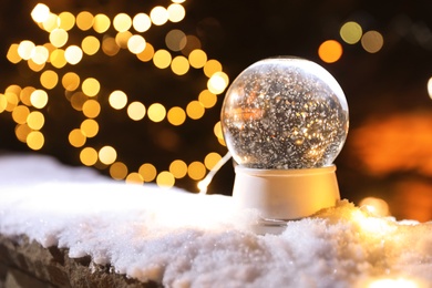 Photo of Snow globe and blurred Christmas lights on background. Space for text