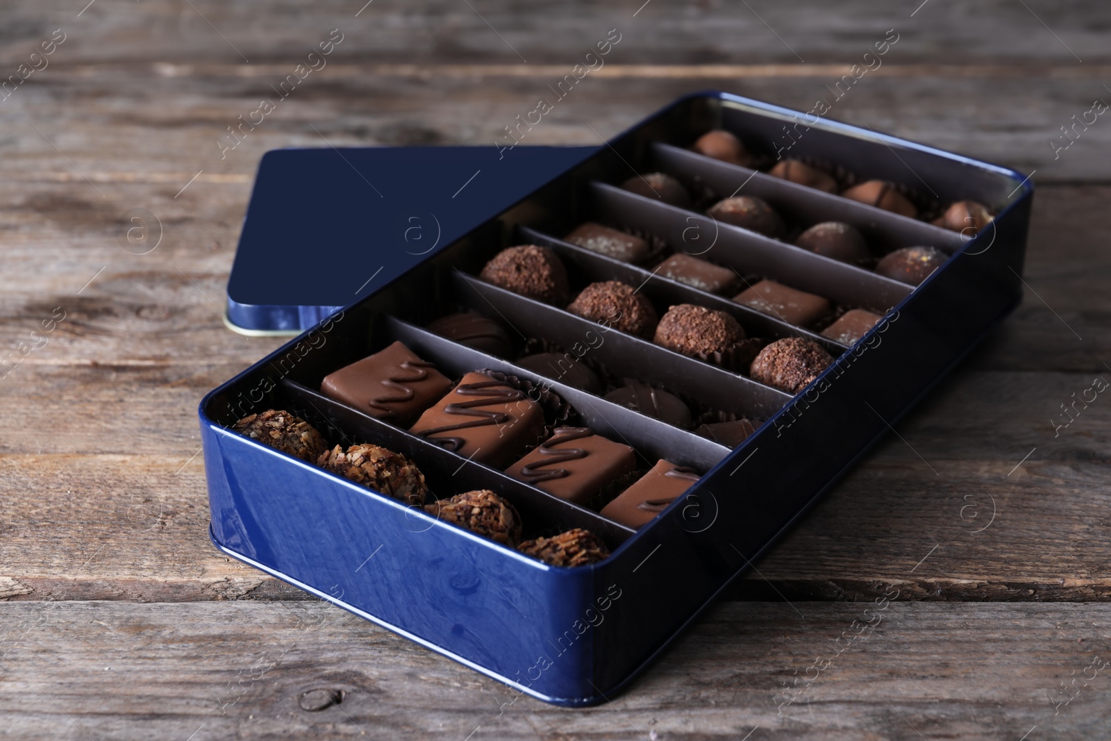 Photo of Metal box with tasty chocolate candies on wooden table