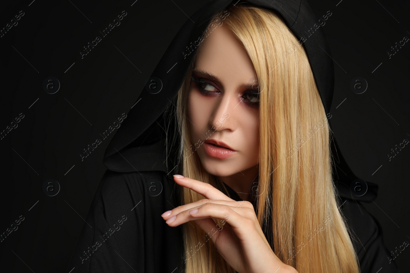 Photo of Witch in black mantle on dark background. Scary fantasy character