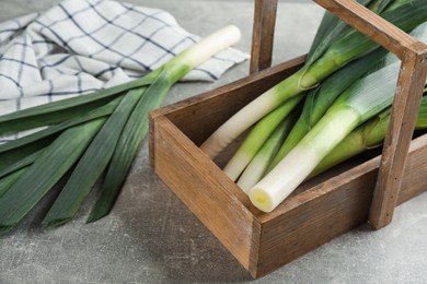 Fresh raw leeks with crate on grey table, closeup