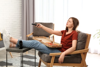 Photo of Lazy young woman with pizza and drink watching TV at home
