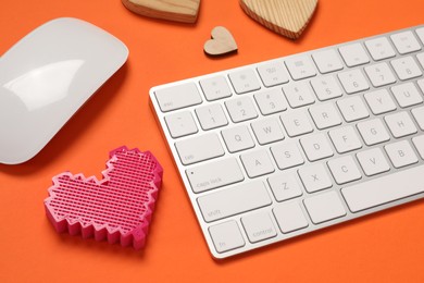 Photo of Long-distance relationship concept. Keyboard, decorative hearts and computer mouse on orange background, closeup