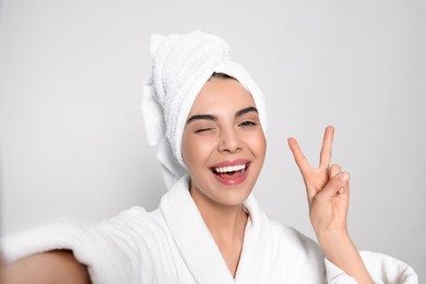 Woman in bathrobe with towel taking selfie on light grey background. Spa treatment