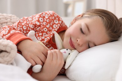 Photo of Cute little girl with toy bunny sleeping in bed at home, closeup