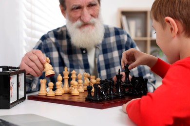 Photo of Grandfather and grandson playing chess at table in room, closeup