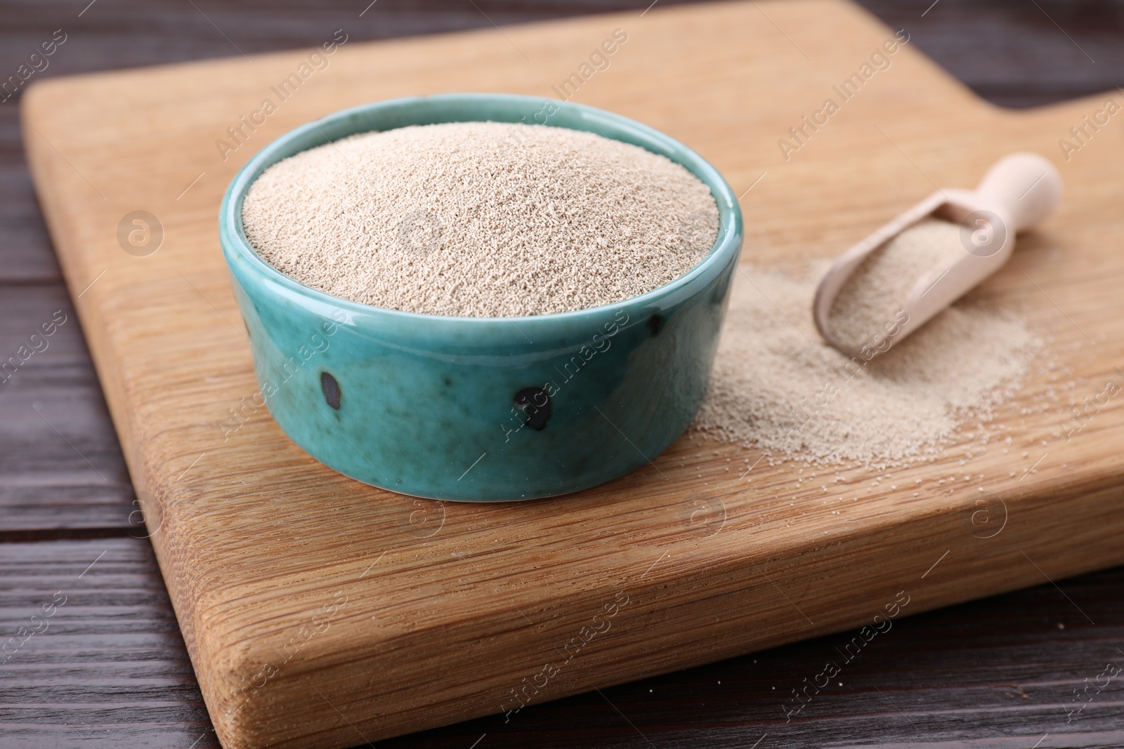 Photo of Bowl and scoop with active dry yeast on wooden table, closeup