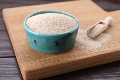 Bowl and scoop with active dry yeast on wooden table, closeup