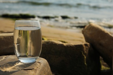 Glass of fresh water on stone near sea, space for text