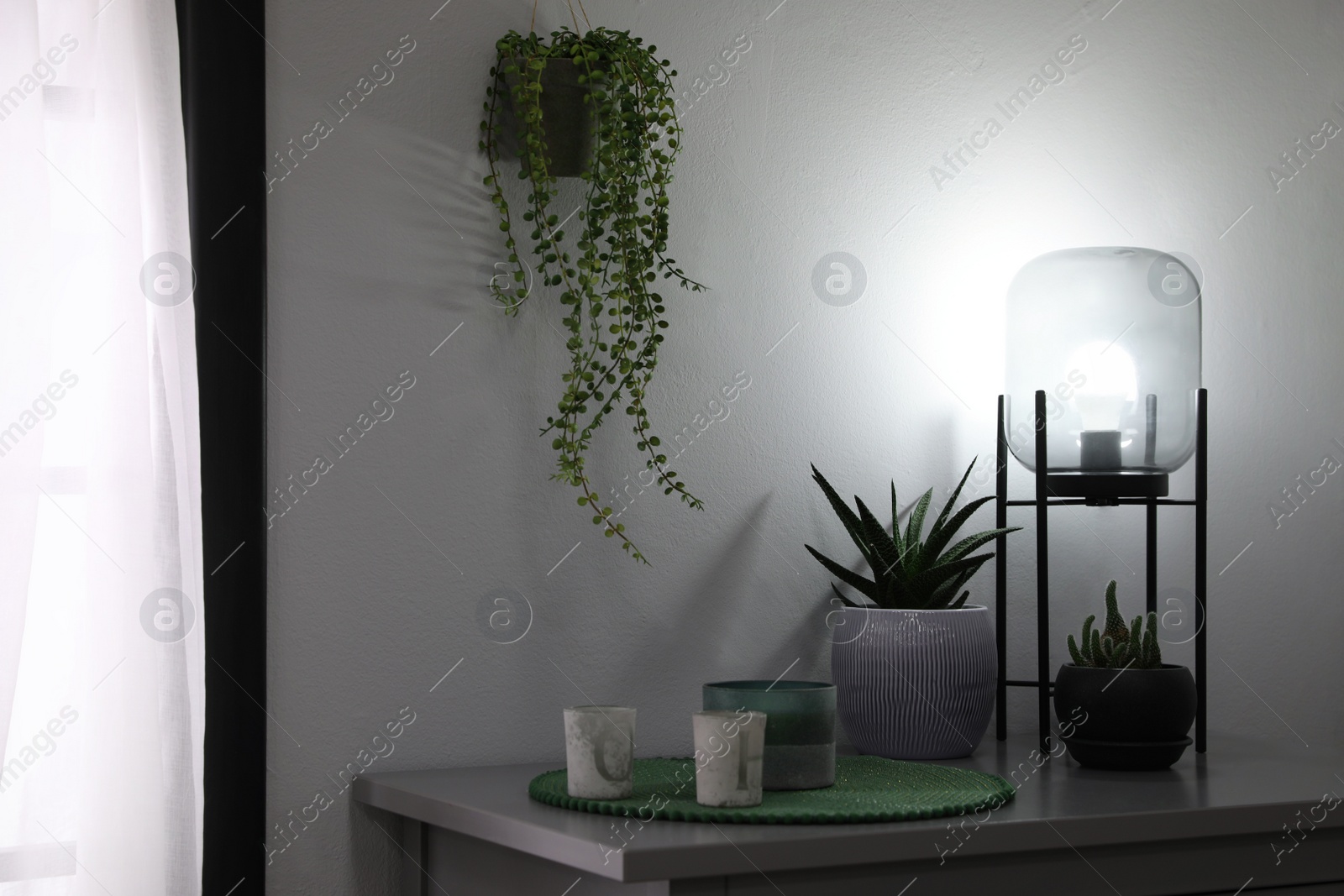 Photo of Stylish lamp, candles and green plants on grey table indoors. Interior design