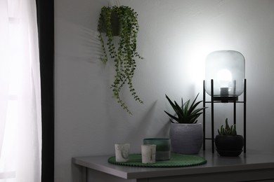 Photo of Stylish lamp, candles and green plants on grey table indoors. Interior design