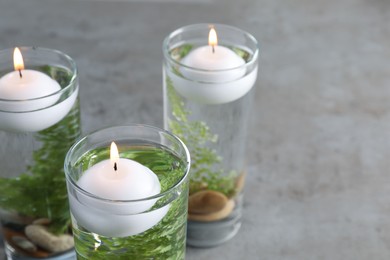 Candles, stones and fern leaves in glass holders with liquid on grey table, closeup