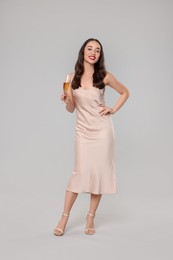 Christmas celebration. Beautiful young woman with glass of champagne on grey background