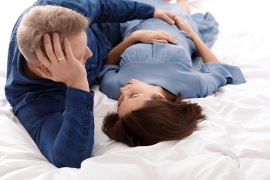 Photo of Young pregnant couple lying on bed at home