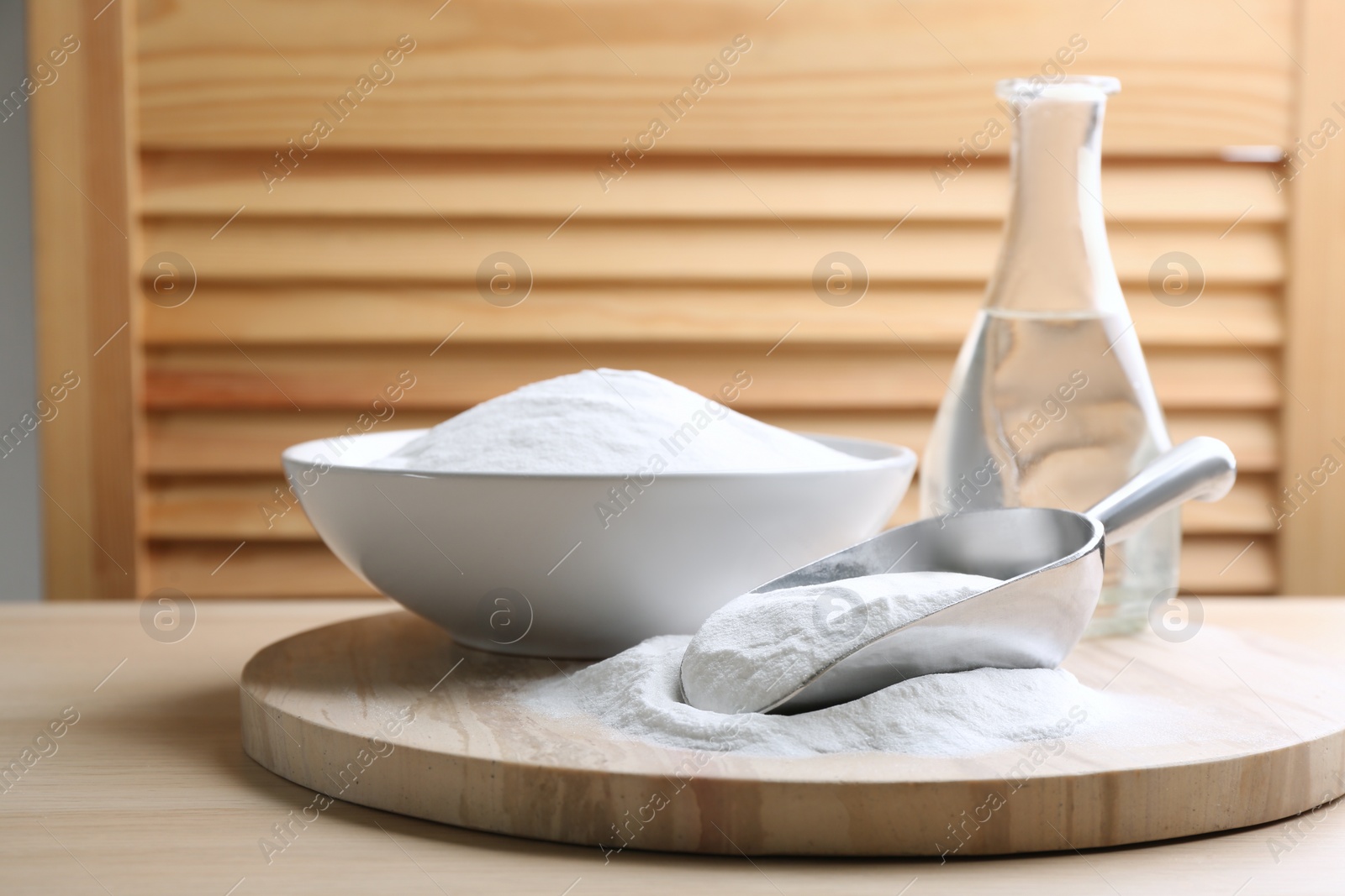 Photo of Baking soda in scoop and bowl on wooden table