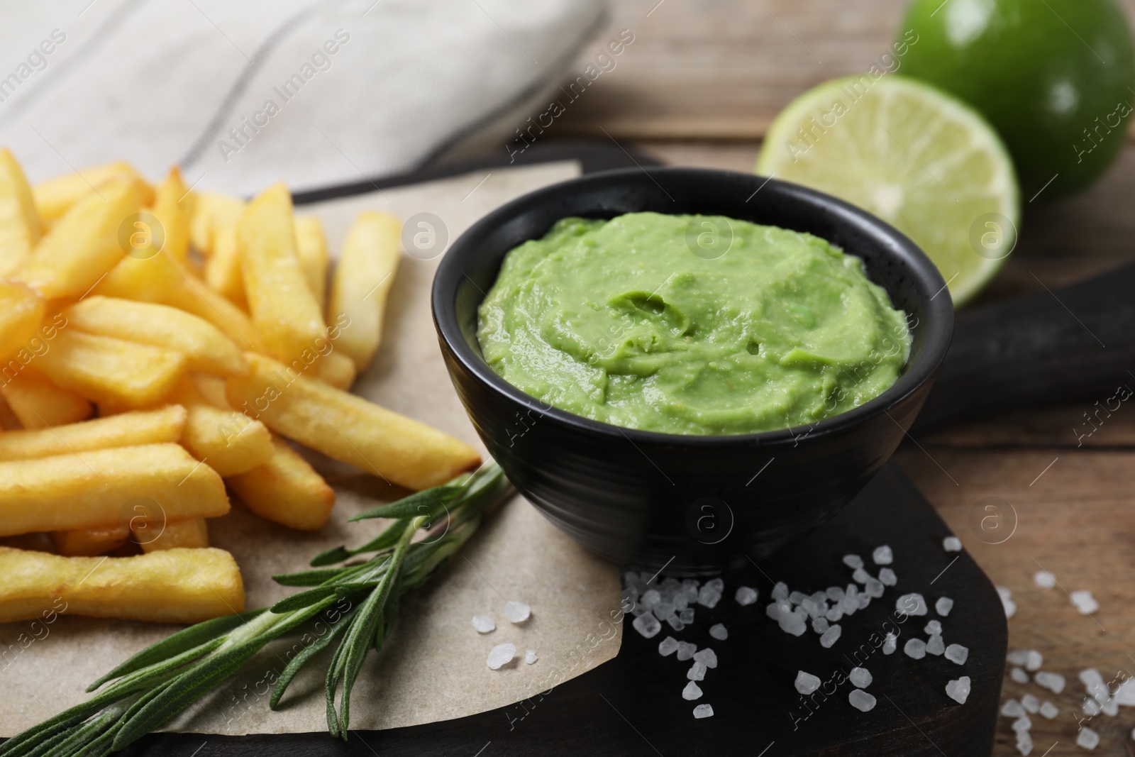 Photo of Serving board with french fries, avocado dip, rosemary and lime served on wooden table, closeup