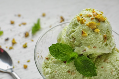 Photo of Delicious green ice cream served in dessert bowl on white table, closeup