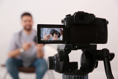 Photo of Young blogger with camera recording video indoors, focus on screen