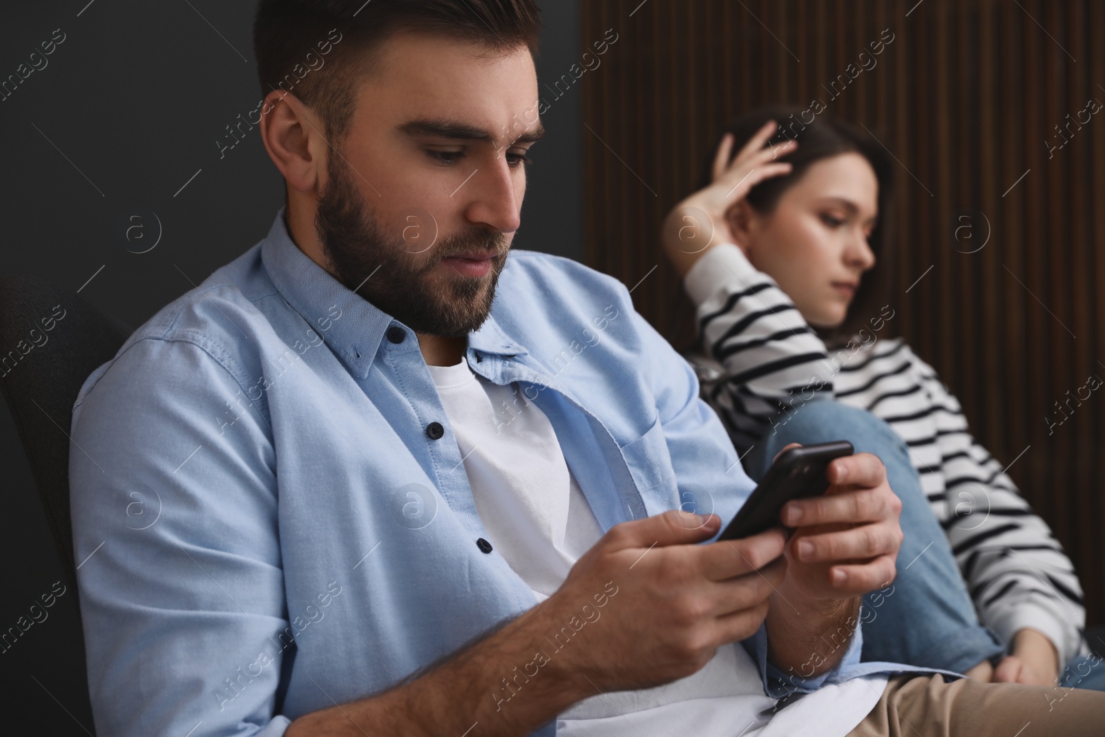 Photo of Young man preferring smartphone over his girlfriend at home. Relationship problems