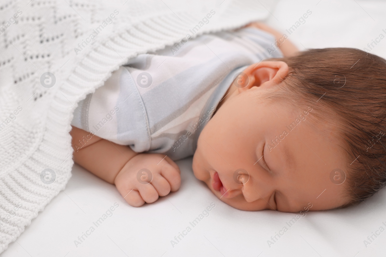 Photo of Cute newborn baby sleeping under white plaid on bed, closeup