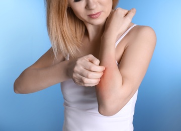 Photo of Woman with allergy symptoms scratching forearm on color background, closeup