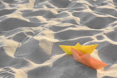 Colorful paper boats on sand outdoors, space for text