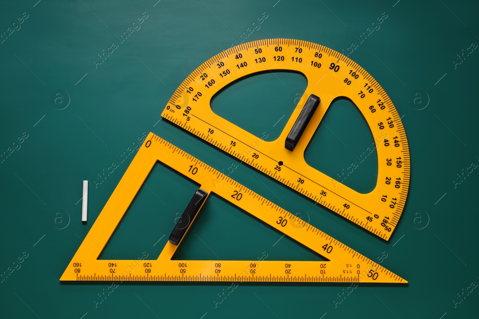 Photo of Protractor, triangle and chalk on green chalkboard, flat lay