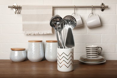 Steel utensils and different dishware on wooden table near white brick wall in kitchen