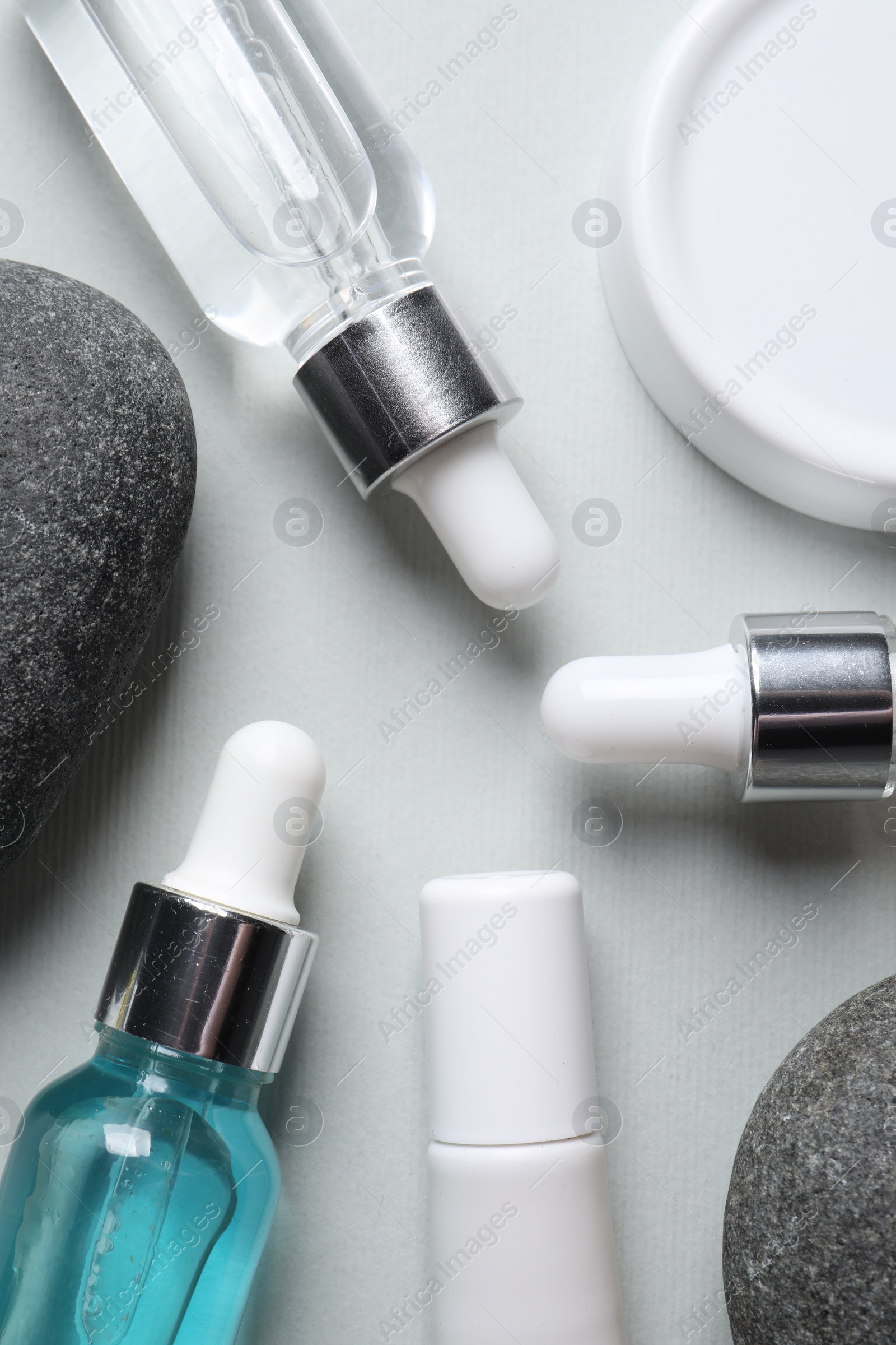 Photo of Bottles with cosmetic serum and stones on light grey background, flat lay