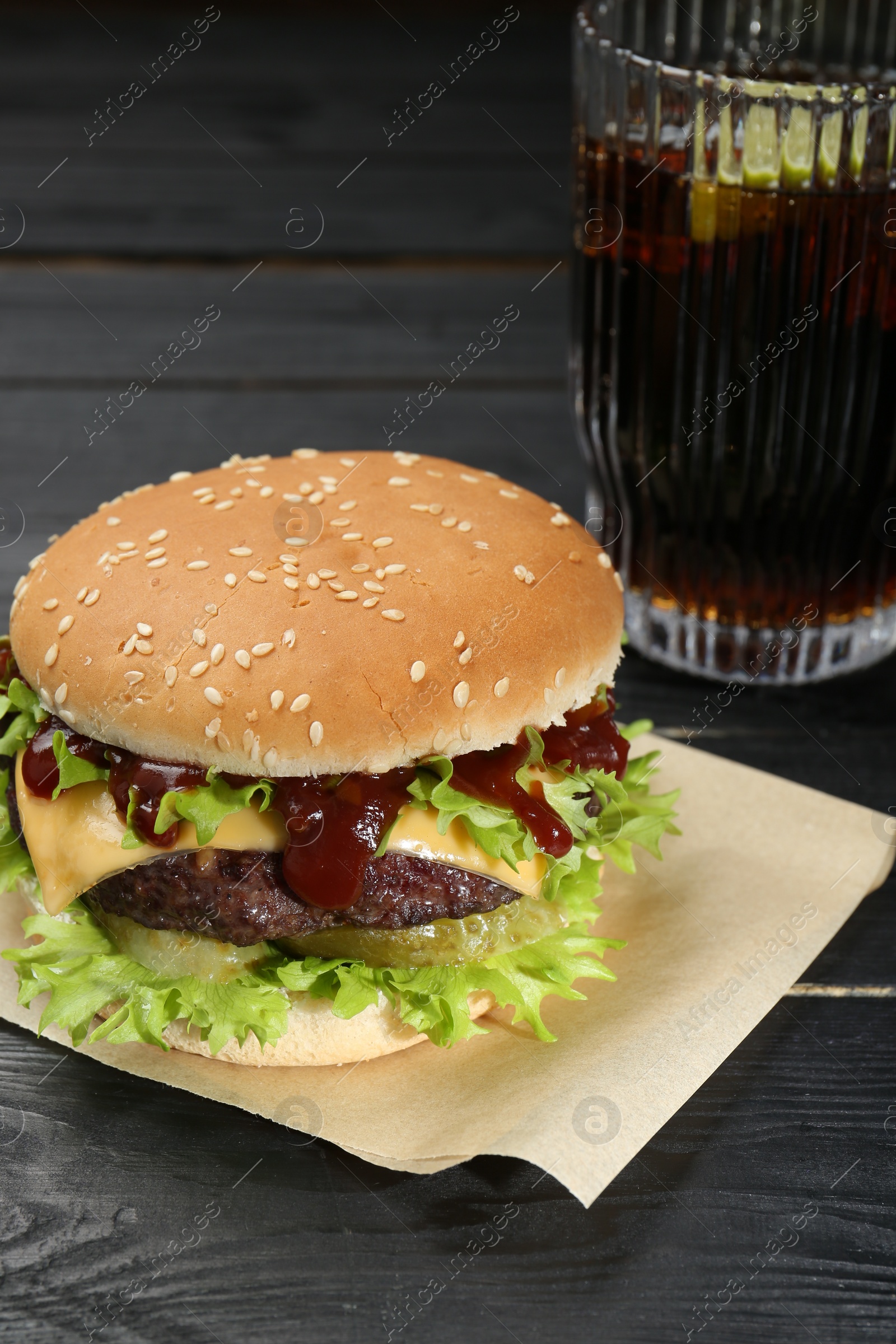 Photo of Burger with delicious patty and soda drink on black wooden table