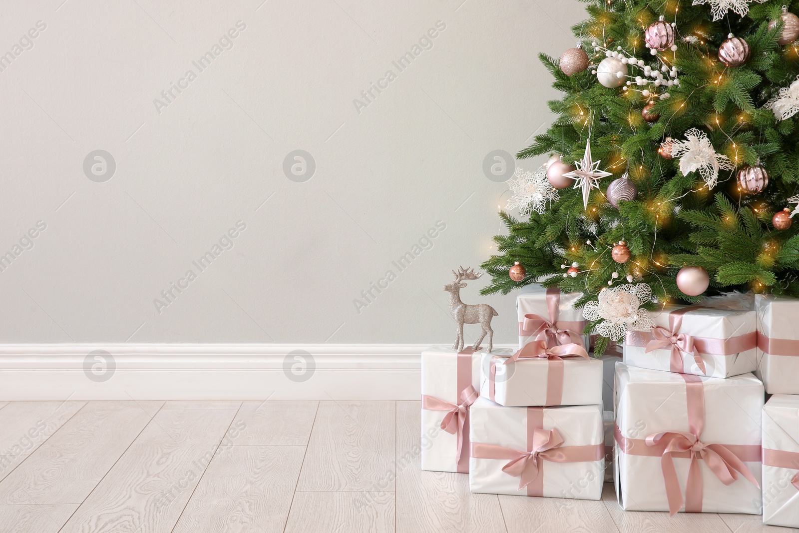 Photo of Beautiful decorated Christmas tree and gifts near light wall. Space for text