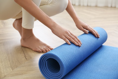 Photo of Woman rolling blue yoga mat indoors, closeup