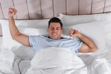 Photo of Man awakening in comfortable bed with white linens, above view