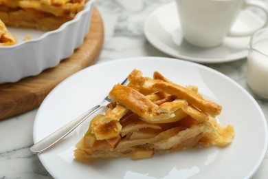 Piece of tasty homemade quince pie and fork on white table, closeup