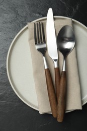 Stylish cutlery, plate and napkin on black table, top view