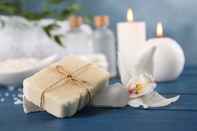 Photo of Soap bars and beautiful flower on blue wooden table, closeup. Retreat concept