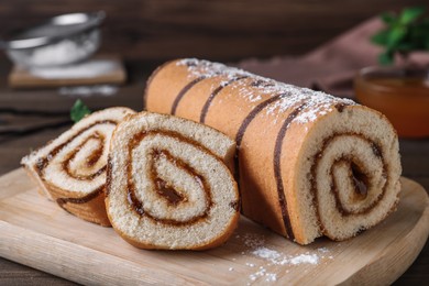 Photo of Tasty cake roll with jam on wooden board, closeup