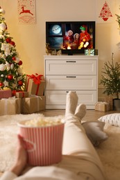 Woman with popcorn watching festive movie on TV in room decorated for Christmas, closeup